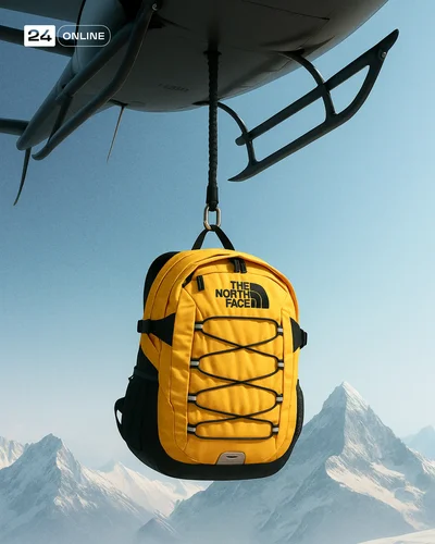 Luxury product suspended beneath helicopter over snowy mountains in cinematic editorial style.